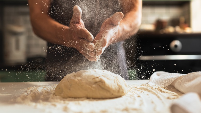 Hands sprinkling flour over dough