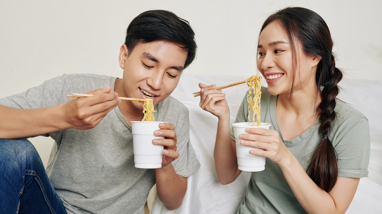 man and woman eating ramen noodles with chopsticks