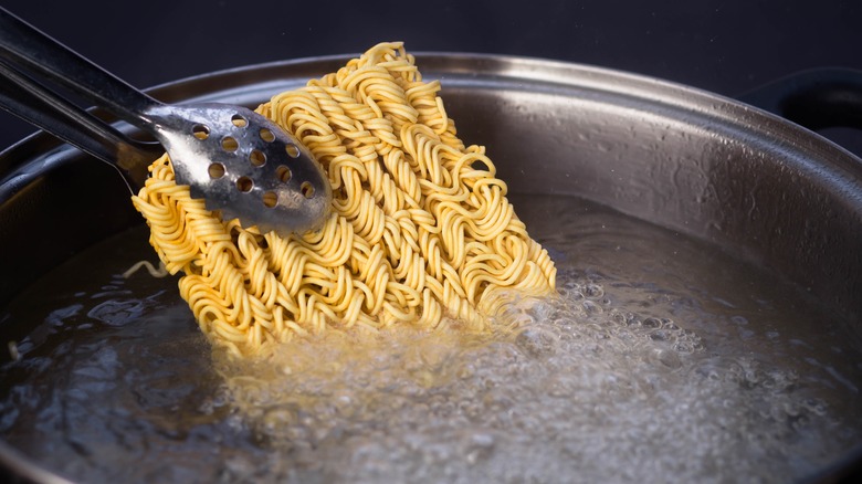 tongs putting instant ramen in a pot