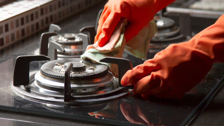 gloved hands cleaning gas stovetop with soft cloths