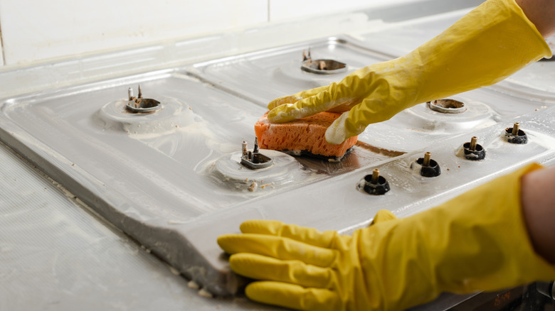 gloved hands cleaning electric stove with coils removed