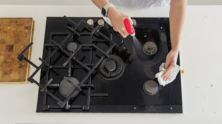 person cleaning gas stove with spray bottle and grates removed