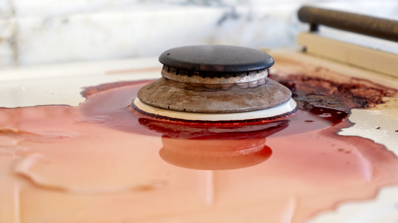 messy liquid spill underneath surface of gas stovetop