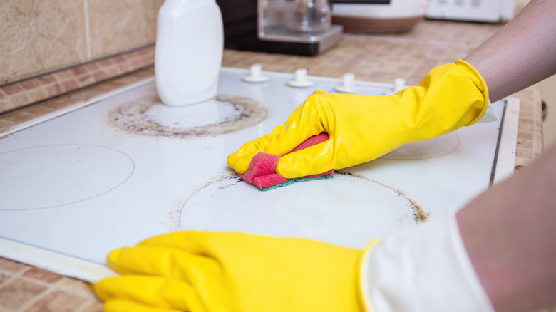 gloved hands using rough side of sponge for cleaning stovetop