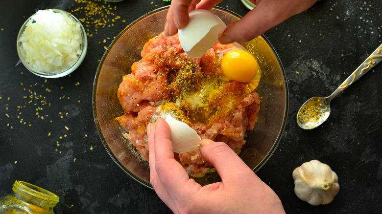 Person cracking egg over meat