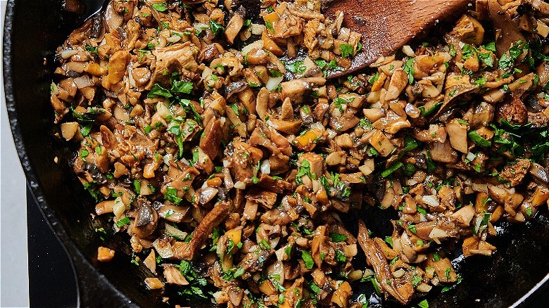 stirring mushrooms and parsley in a skillet