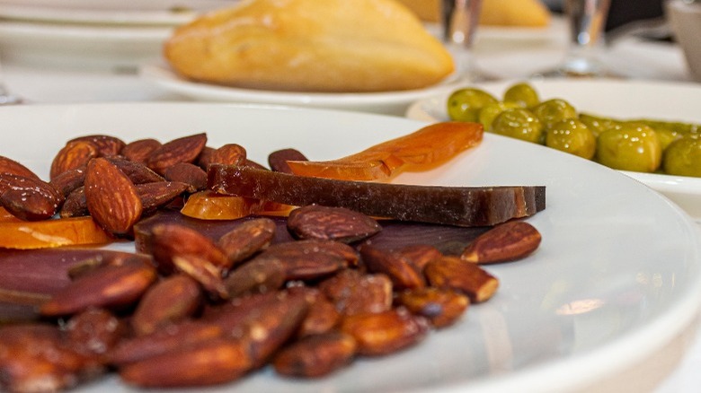 Thick slices of mojama atop a plate of almonds with bread and olives