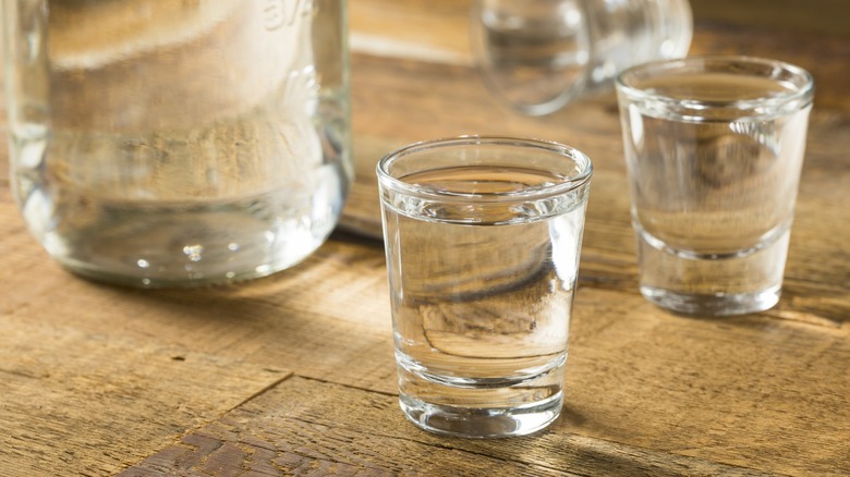 Shots of moonshine next to a bottle