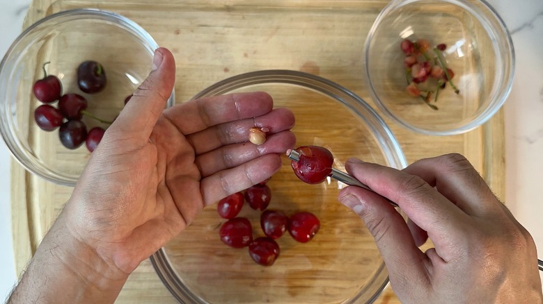 hand pitting cherries over cutting board