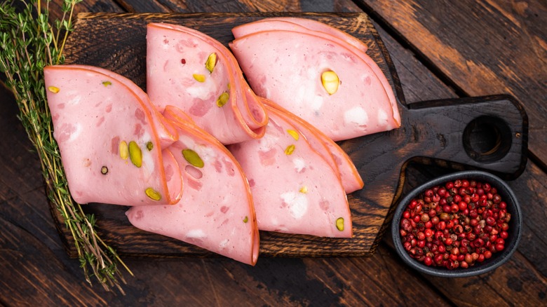 Mortadella slices neatly folded on a charcuterie board beside bowl of red pepper berries and rosemary