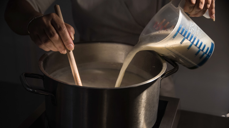 cook pouring milk into a pot with a ladle