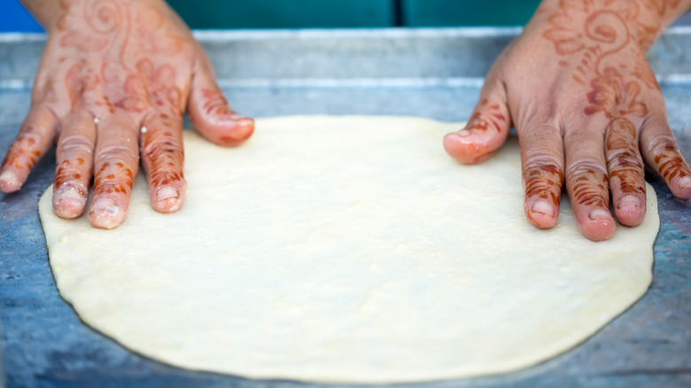 Hands flattening msemen dough