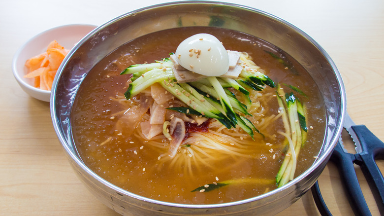 bowl of naengmyeon with scissors and radish kimchi