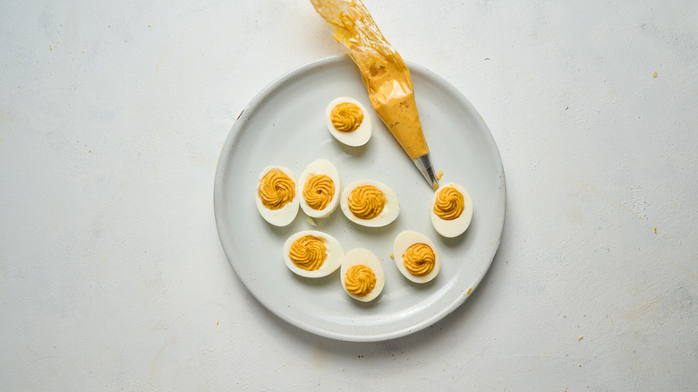 deviled eggs on white plate with piping bag of yolk