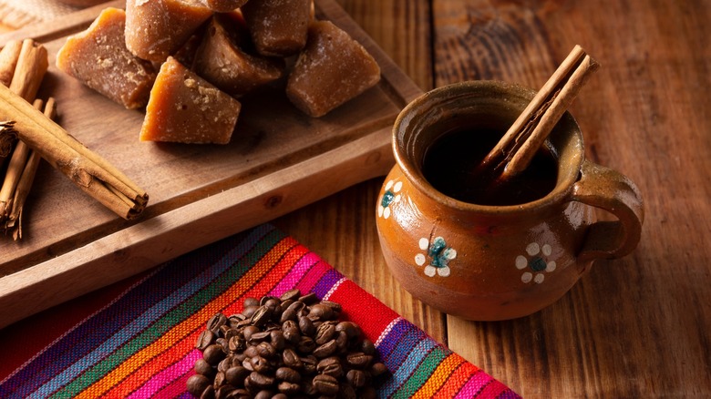 Mexican cafe de olla in a clay jar with cinnamon sticks next to ingredients