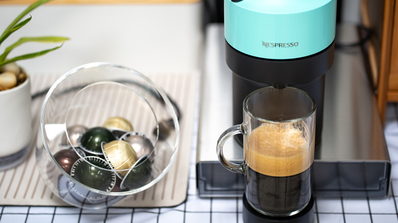 Nespresso machine making espresso next to a bowl of pods