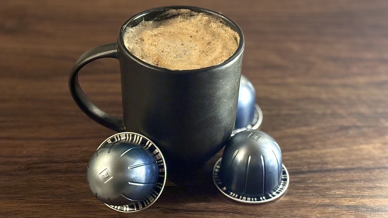 Coffee cup with Nespresso cold brew, surrounded by three blue cold brew pods