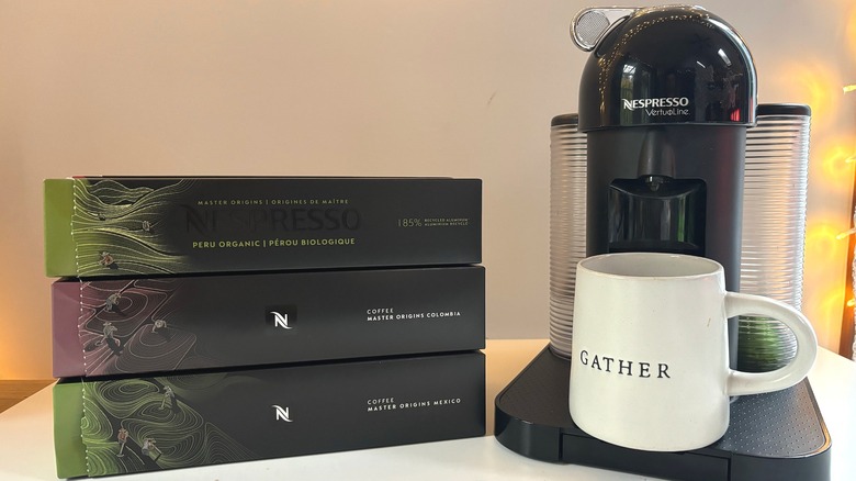 Three boxes of Nespresso pods next to a black Vertuo machine and a mug