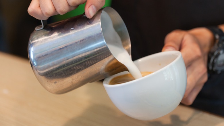 Close-up of barista pouring steamed milk into a mug