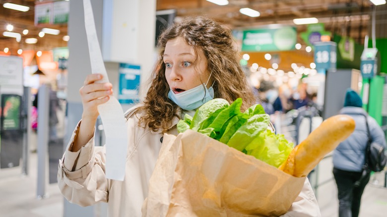 woman looks at a grocery receipt in shock