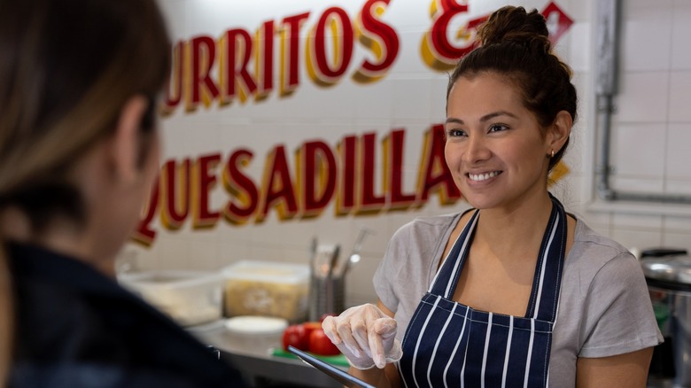 A smiling woman taking an order at a Mexican restaurant