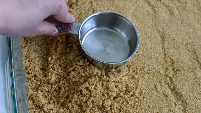 crust being pressed into a pan with a measuring cup