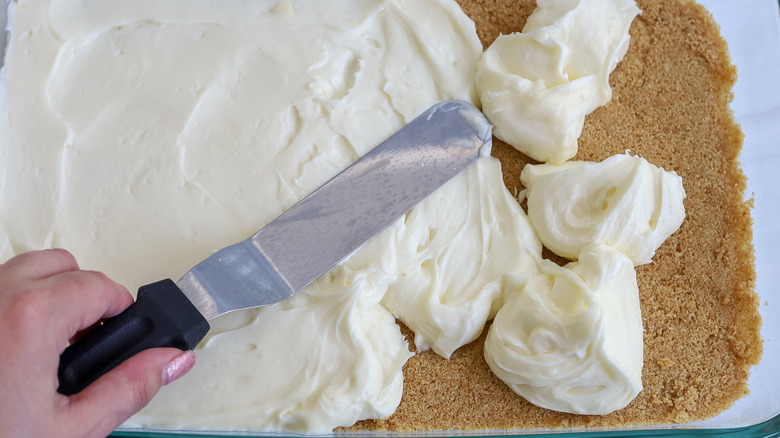 cream cheese filling being spread over a graham cracker crust