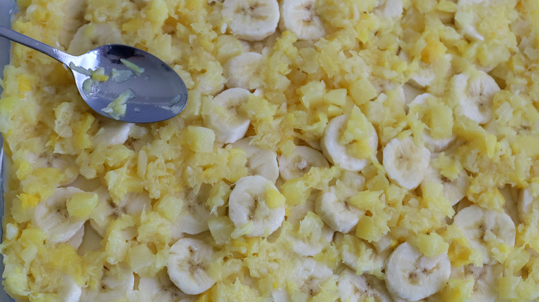 crushed pineapple being spooned over bananas in a pan