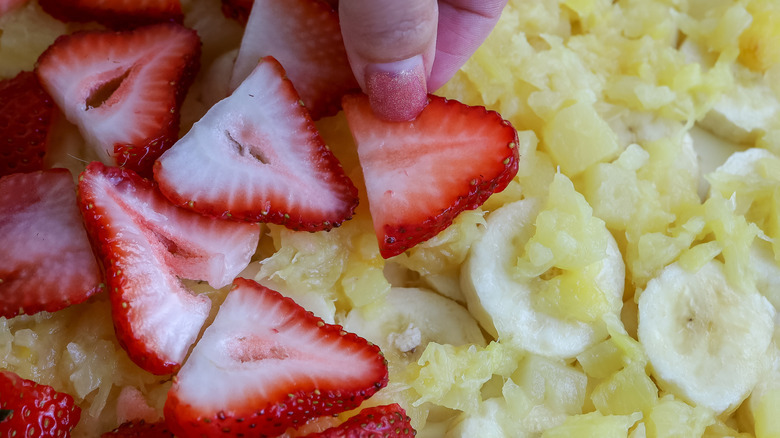 strawberries being placed over bananas and pineapple