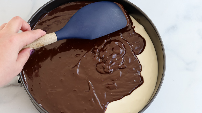 spreading chocolate topping on cheesecake