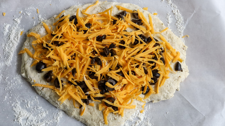 sliced olives and shredded cheese on dough