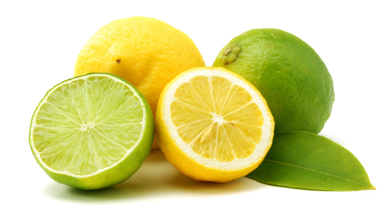 Whole and sliced lemons and limes on a white background