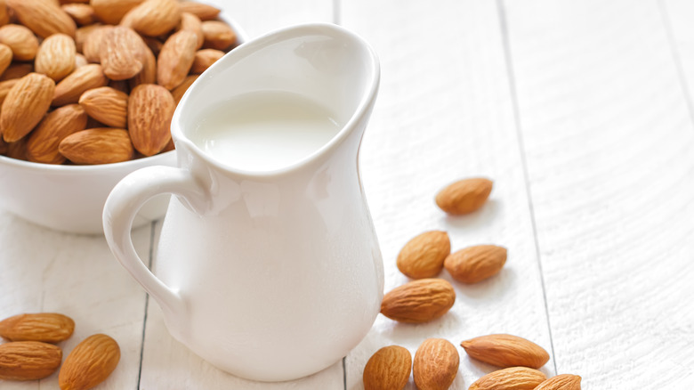 Almond milk in a jug with whole almonds in the background