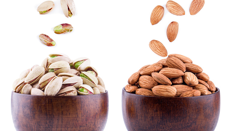 Almonds and pistachios falling into bowls, side by side