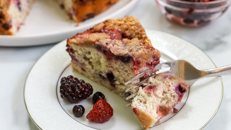 a slice of summer berry buckle on a plate being cut into with a fork
