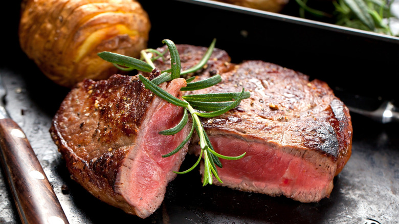 A steak that has been sliced, showing off a medium rare cook, with a sprig of rosemary