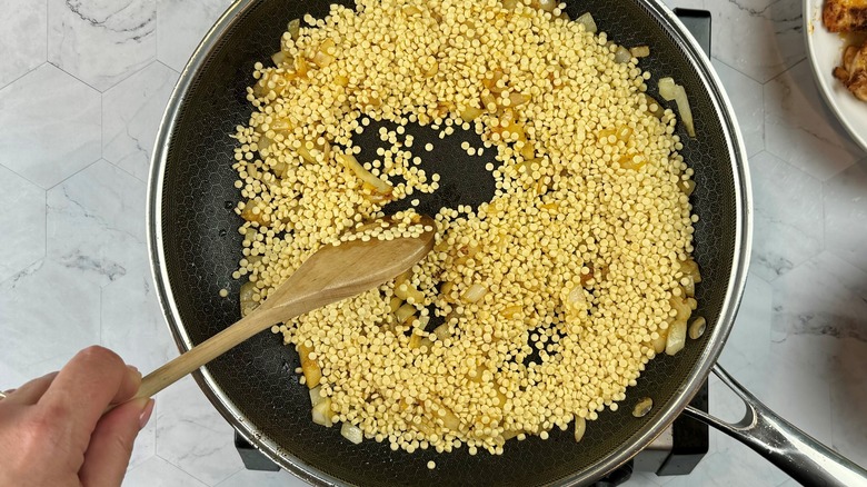 hand stirring couscous in pan