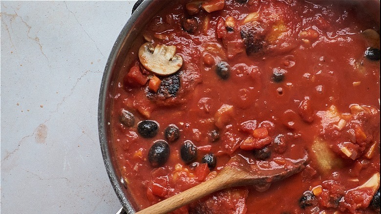 spoon stirring tomatoes with olives