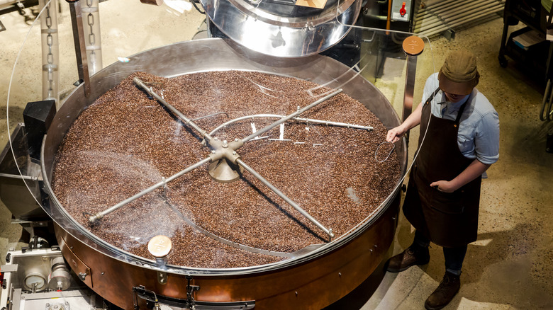 A coffee roaster works a pan of roasting beans