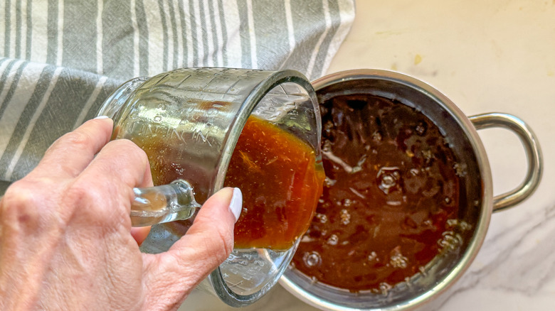 hand adding sauce to pot