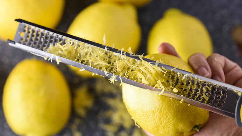 Lemon zest on a grater next to whole lemons