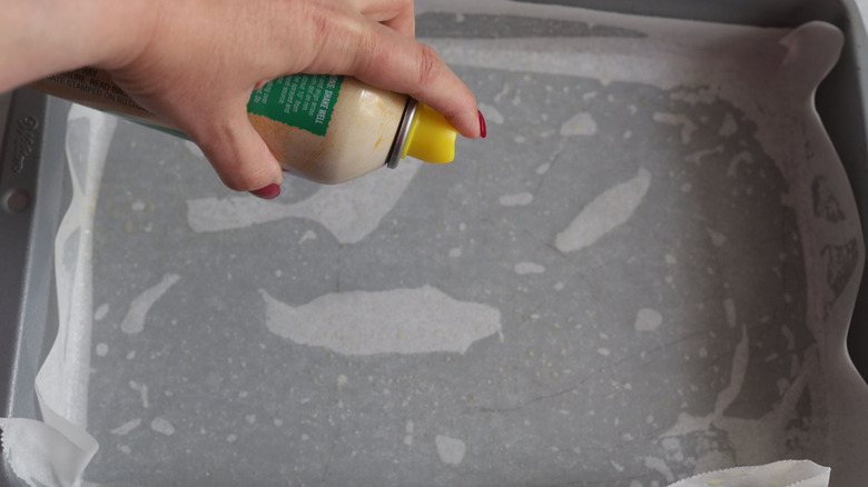 Hand spraying parchment-lined baking dish with cooking spray