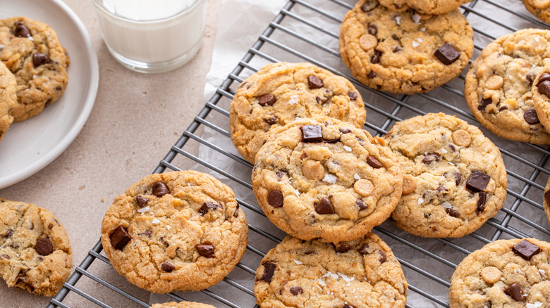 Chocolate chip cookies cooling on a rack next to a plate and a glass of milk