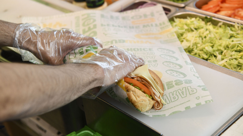 Subway sandwich artist assembling a sandwich