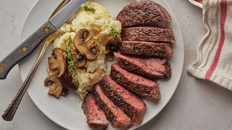 Sliced steak with mushrooms and potatoes on plate