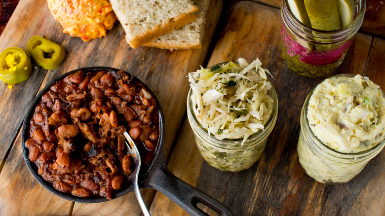 Baked beans, coleslaw, and pickles on cutting board