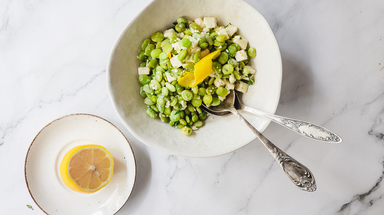 lima beans and feta in bowl with two spoons and lemon half