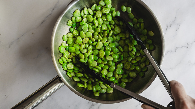 mixing lima beans in pan with tongs