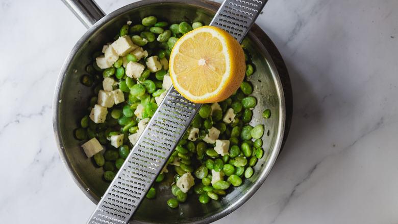 Adding lemon zest to lima beans in pan