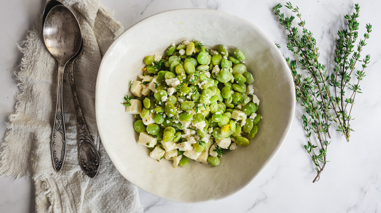 lima beans and feta in bowl with two spoons and thyme